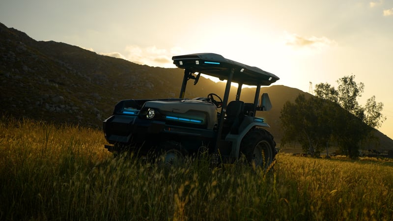 MK-V electric tractor in a grassy field backlit by sunrise peaking over the mountains. Image is awash in gold colors and soft lighting. 