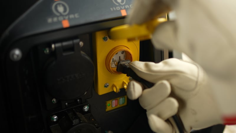 Farmer's gloved hand plugging a tool into portable power source on MK-V electric tractor.