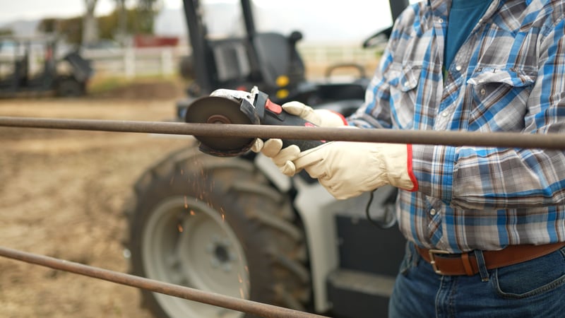 Closeup of farmer using an electric tool powered from electric tractor battery. MK-V electric tractor in fuzzy focus in background, the power source. 