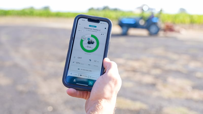 A hand is holding a cell phone showing MK-V's electric tractor battery status. 